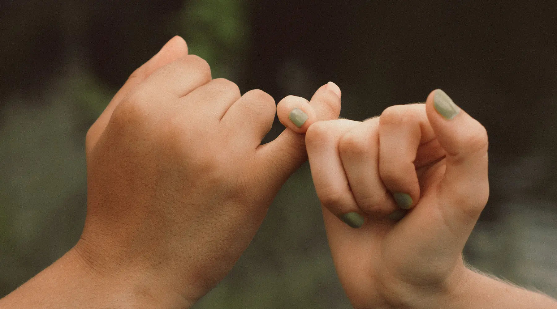Two hands making a pinky promise against a blurred natural background, symbolizing trust, commitment, and friendship.