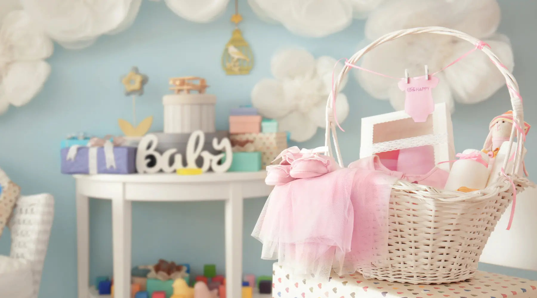 White wicker baby shower gift basket with pink baby items and pastel party decor