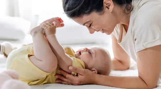 Mother and baby sharing playful moment as mom gently holds smiling baby's feet