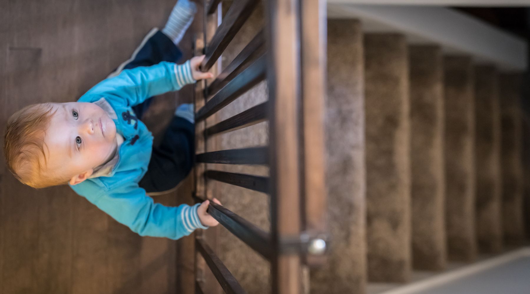 Toddler climbing a staircase while holding onto the railing for support.