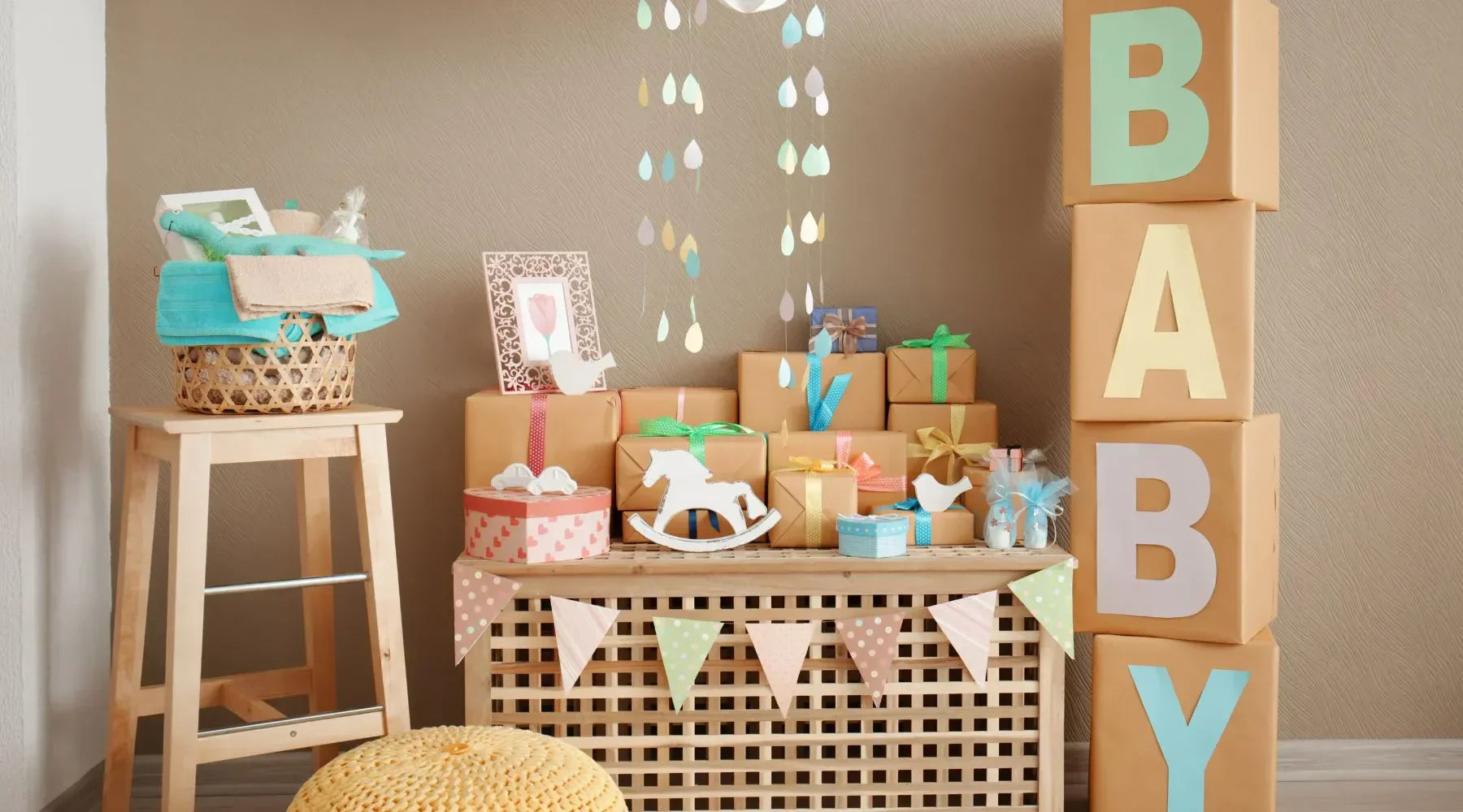 A beautifully decorated baby shower display with gift boxes, a mobile, and festive decor featuring the word "BABY" in colorful letters.