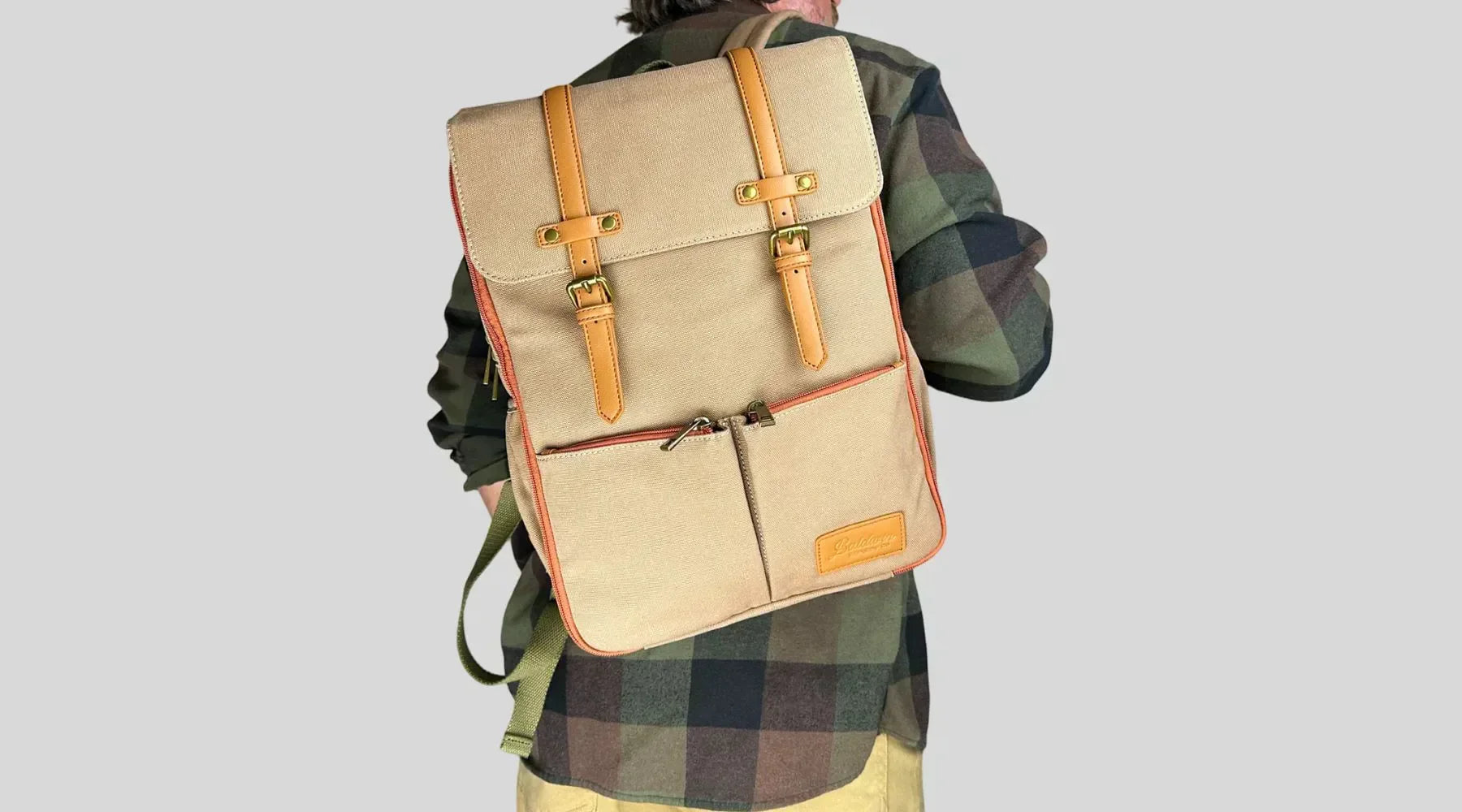 Man in plaid shirt carrying beige canvas diaper backpack with leather straps and buckles