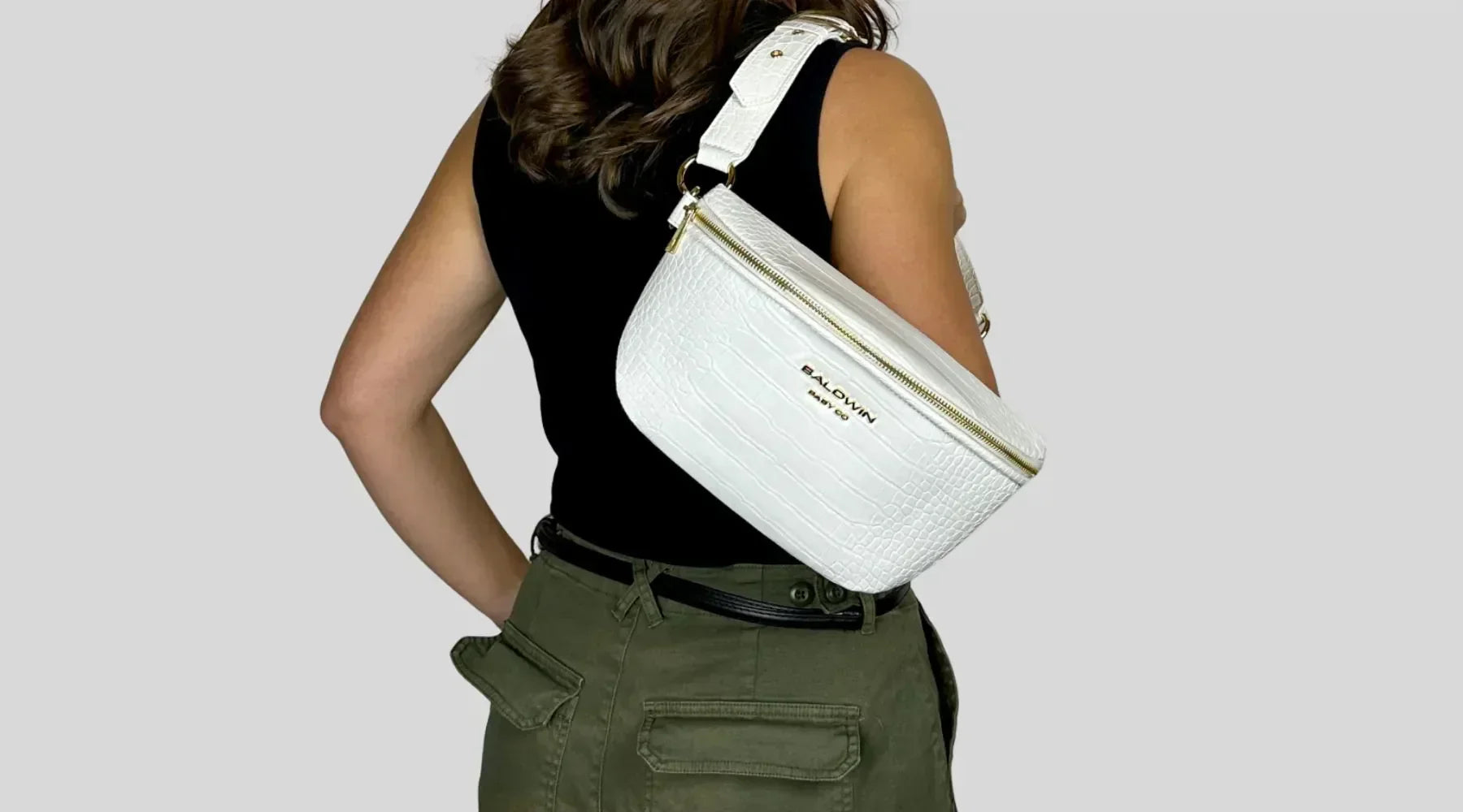 Woman in black top and olive pants wearing white croc-textured belt bag with gold hardware
