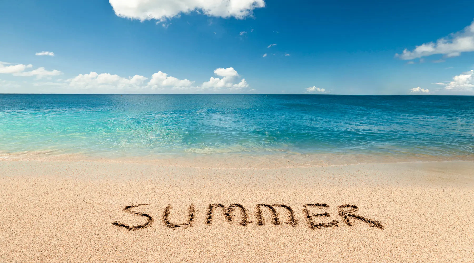 Beach scene with "SUMMER" written in sand, clear blue water, and golden shoreline