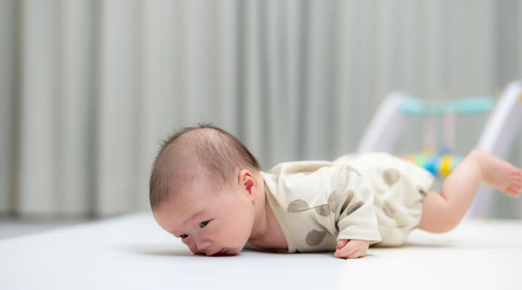 A newborn baby on a white surface, struggling to lift their head during tummy time, showing the early stages of muscle development.