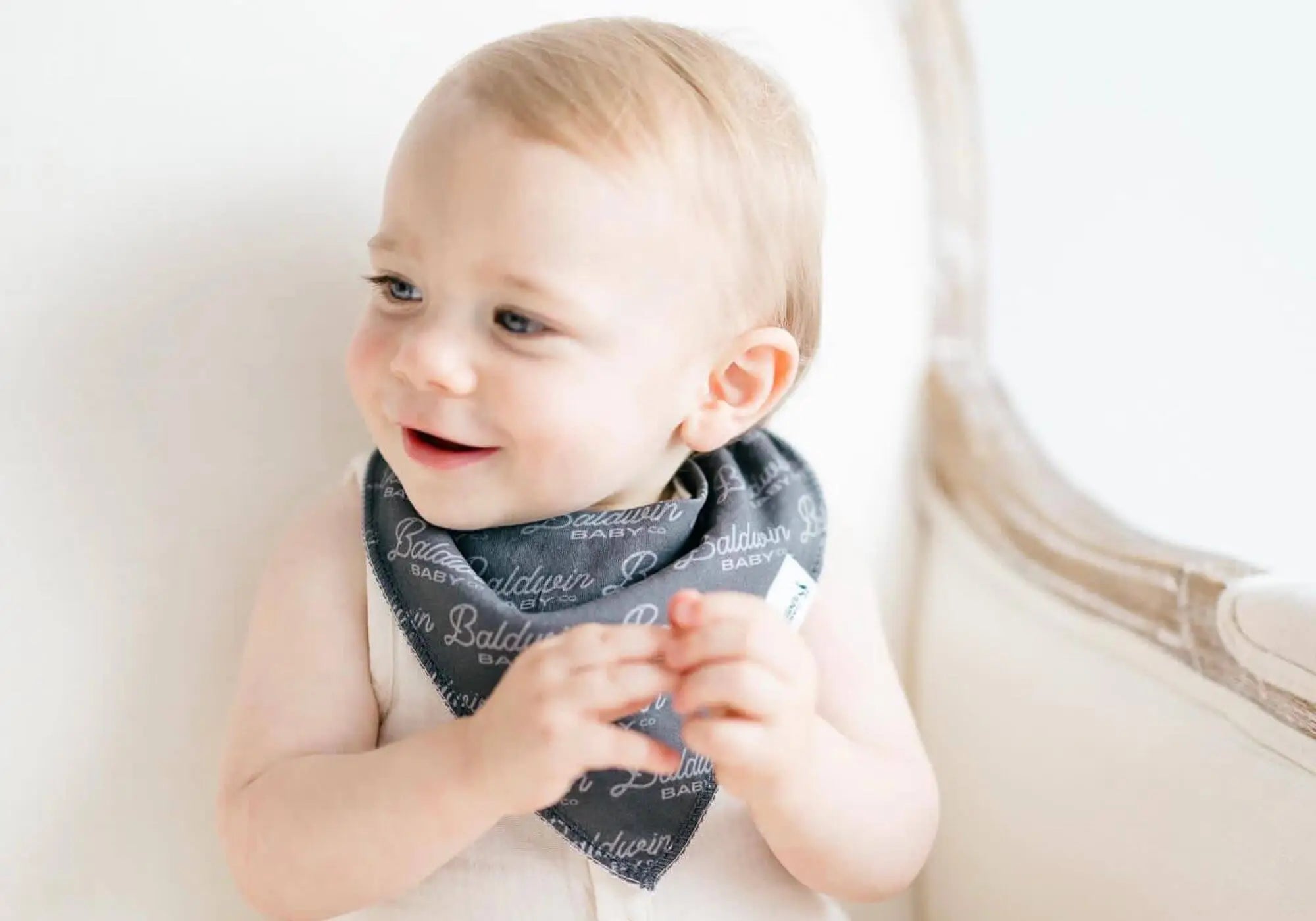 Baby boy wearing charcoal gray bib with Baldwin Baby Co logo printed on it in a lighter gray