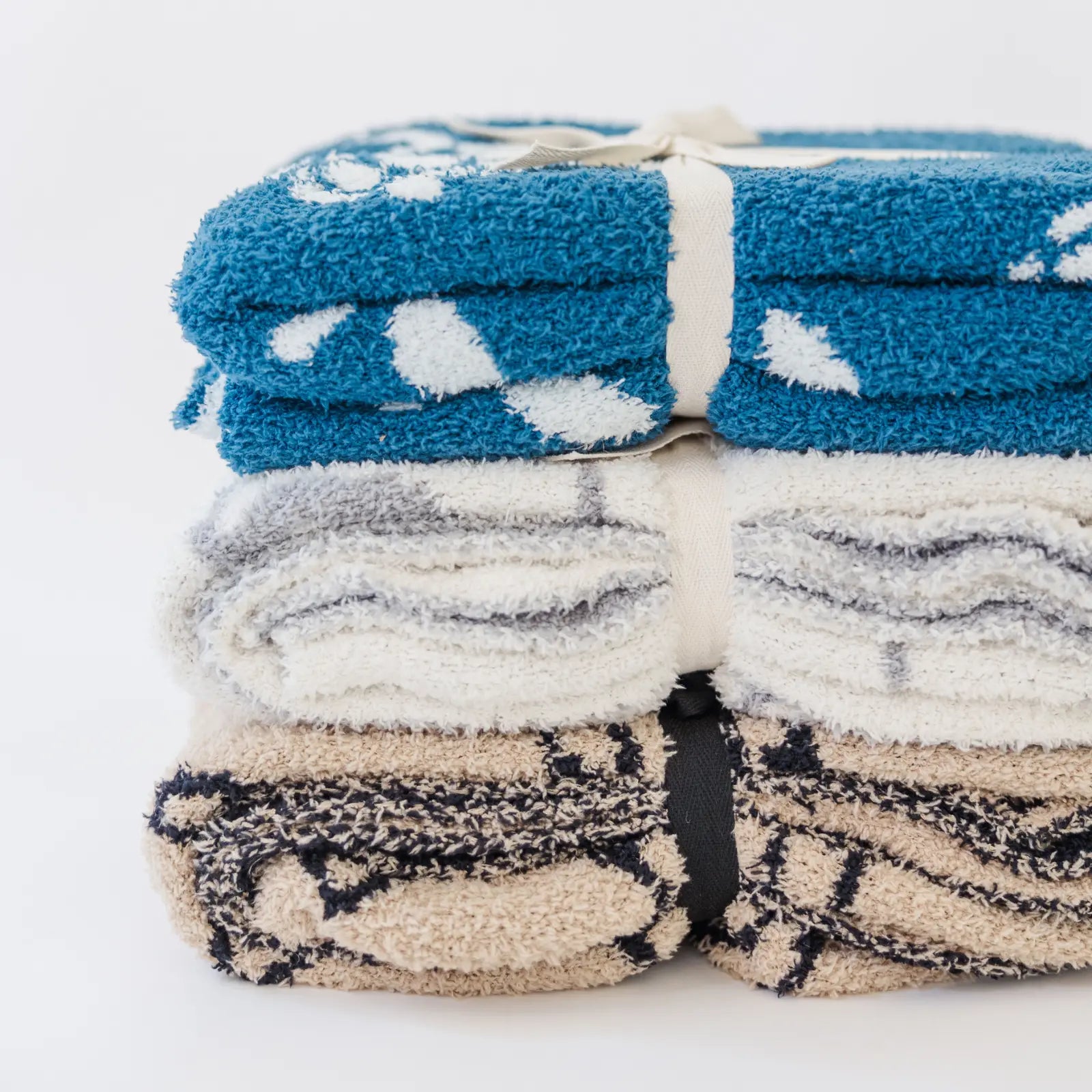 Stack of three folded baby blankets in blue, gray, and beige with assorted patterns