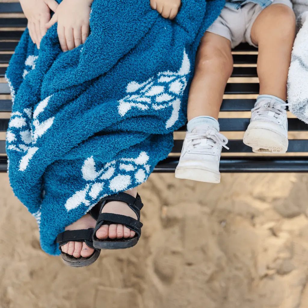 Kids’ feet on bench covered with blue blanket featuring white sea turtle pattern