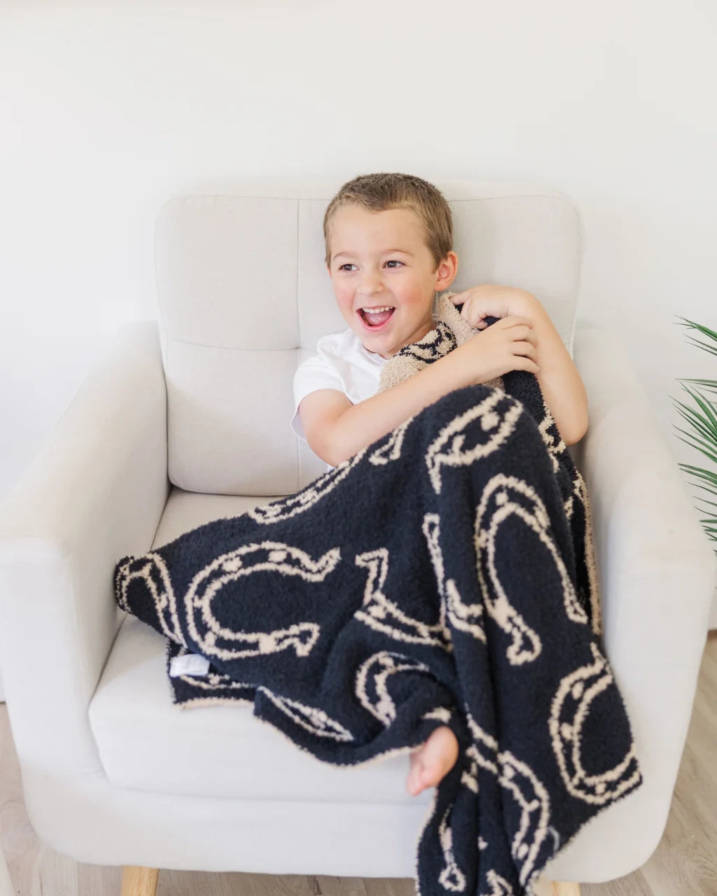 Smiling child wrapped in cozy blanket with black horseshoe print, seated in chair