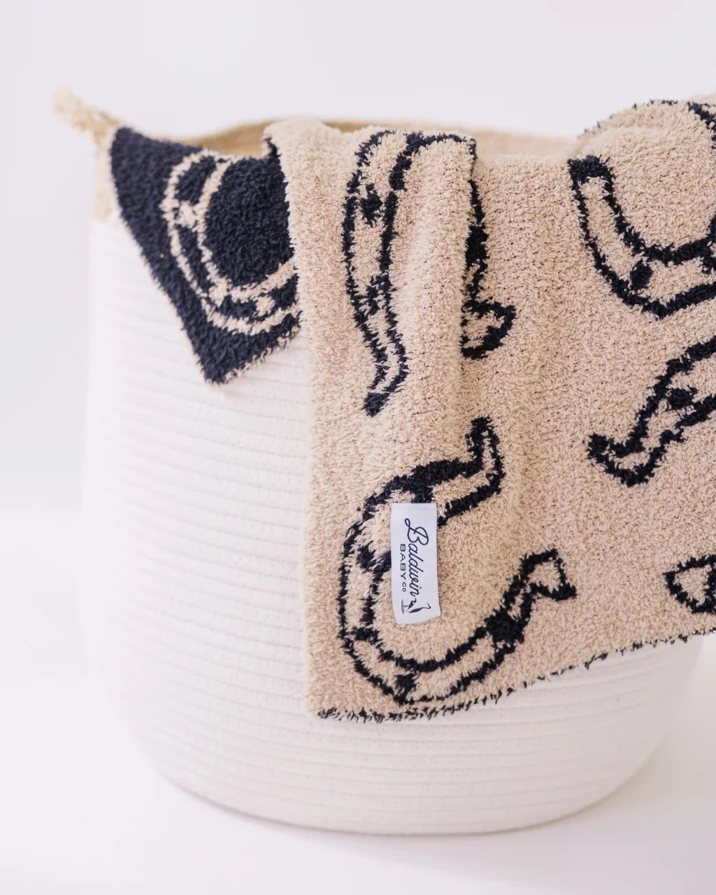 Horseshoe-print baby blanket draped over white rope basket for a decorative touch