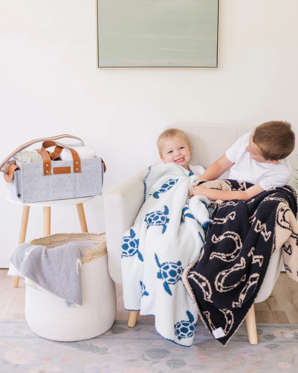 Two kids cuddling with baby blankets featuring blue sea turtles and black horseshoe prints