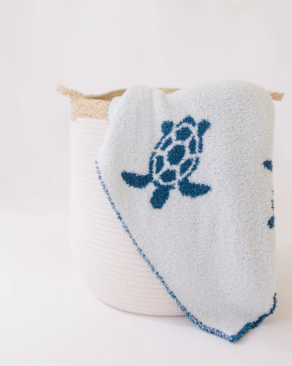 Sea turtle print blanket draped over white rope basket with corn husk handles