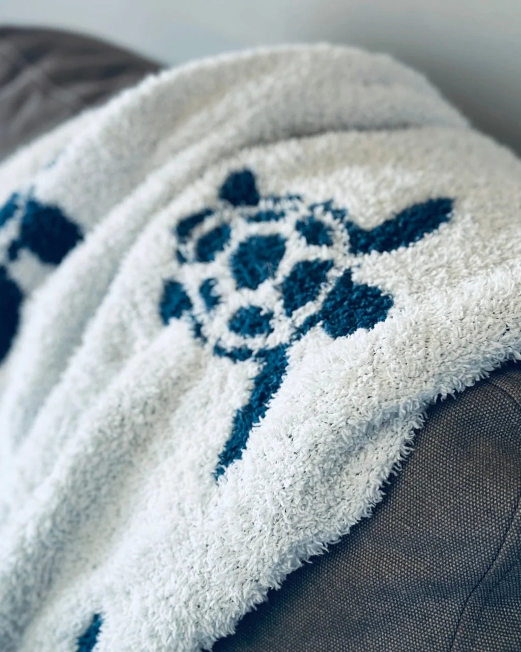 Close-up of blue and white Sea Turtle Blanket on gray chair with detailed turtle pattern
