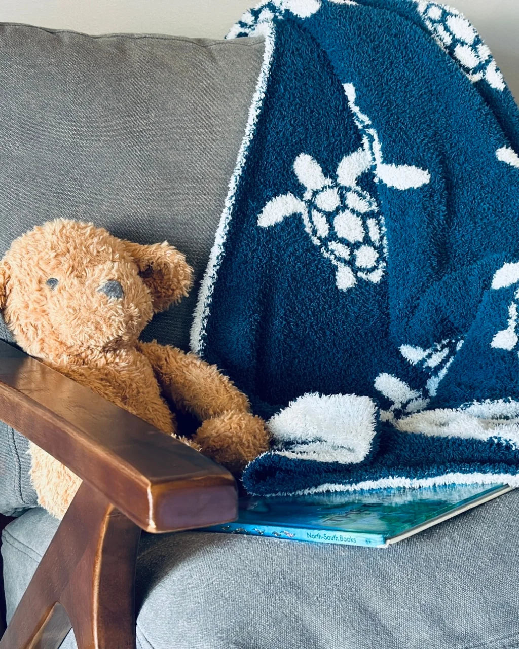 Sea Turtle Baby Blanket on gray chair with teddy bear and book in cozy nursery scene