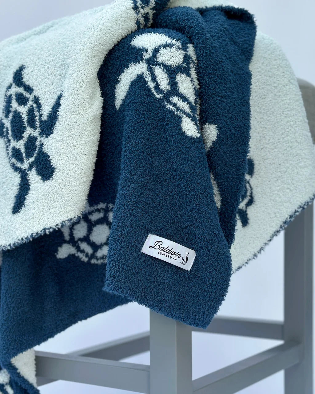 Close-up of blue and white Sea Turtle Baby Blanket on gray stool with turtle pattern