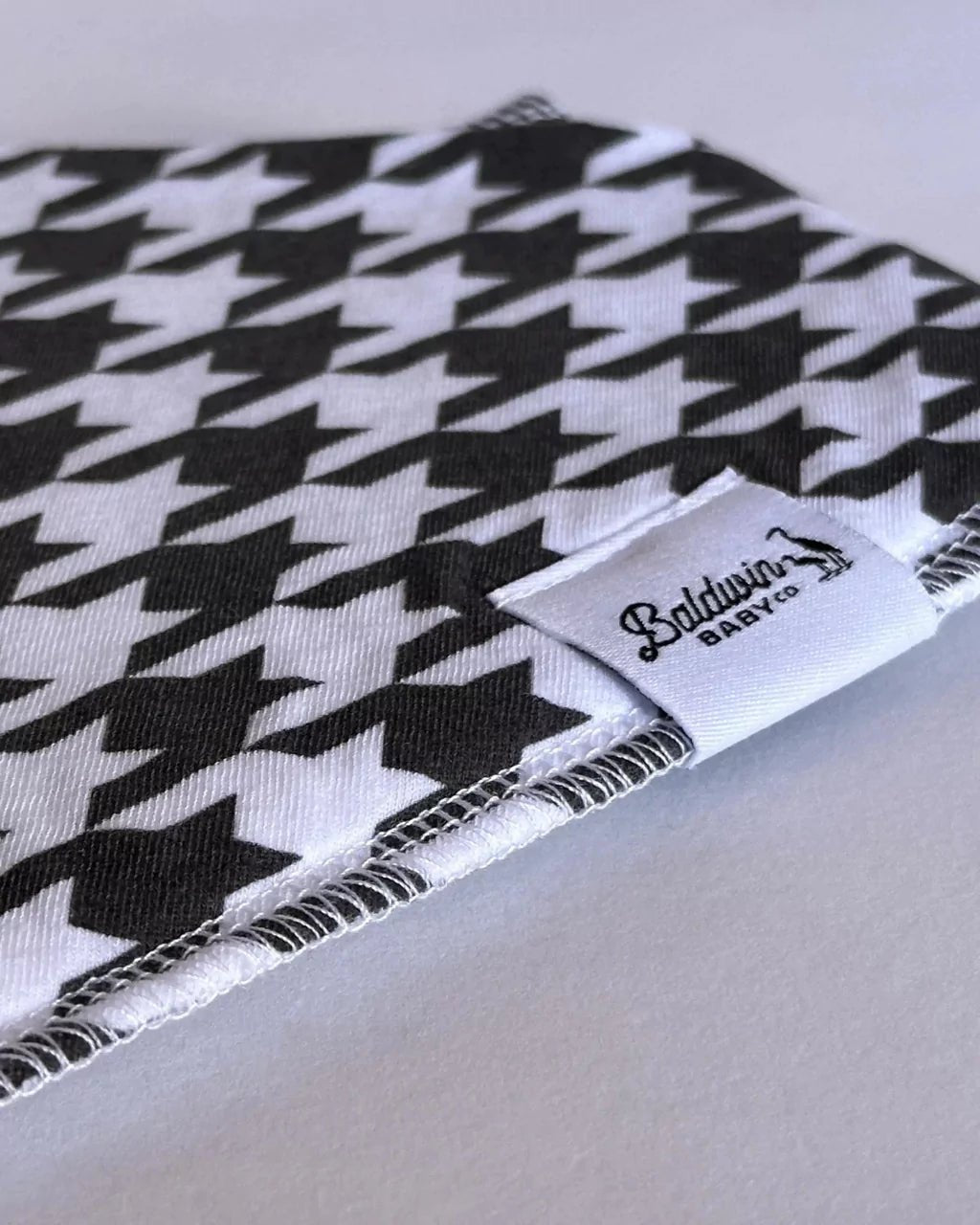 Close up of a traditional white and black houndstooth pattern bandana bib with a white Baldwin Baby Company logo tag