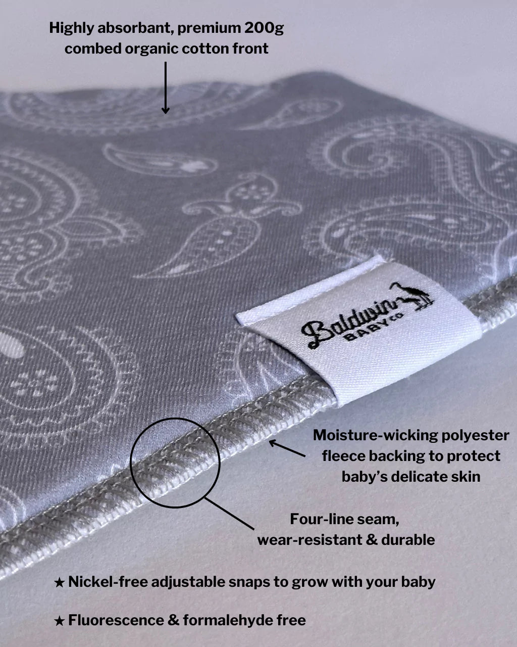 Close up of gray with white paisley bandana bib with a white Baldwin Baby Company logo tag