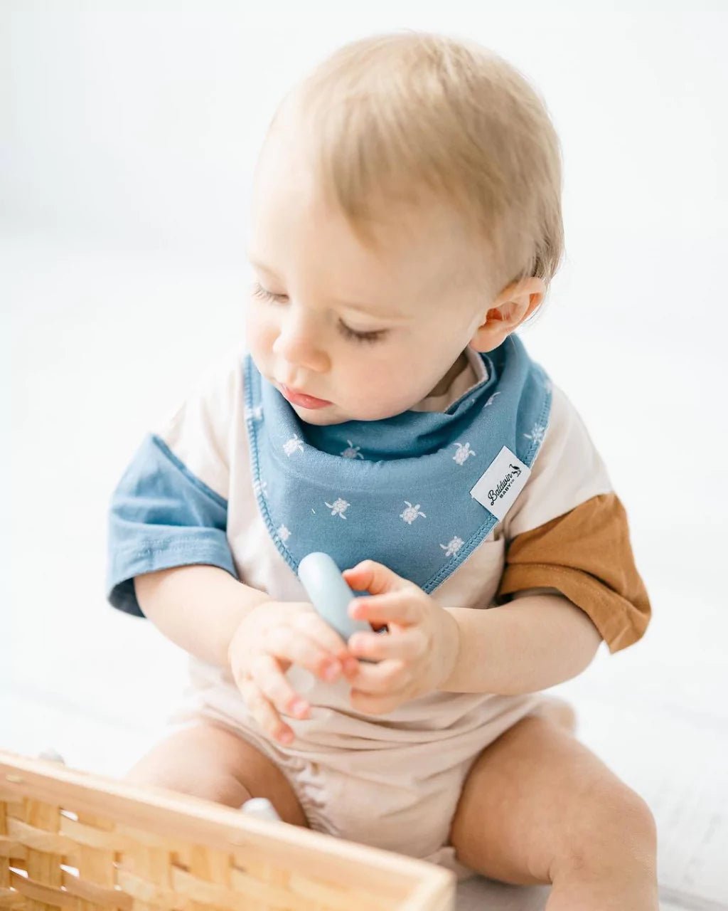 Toddler boy wearing a light blue bandana bib with sea turtles by Baldwin Baby Co