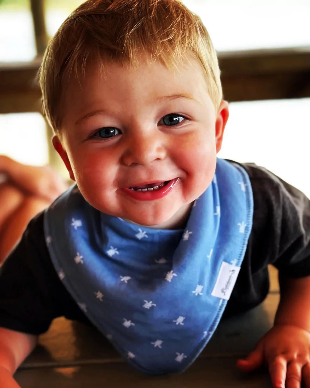 A smiling little boy wearing a blue bandana bib with a white sea turtle pattern