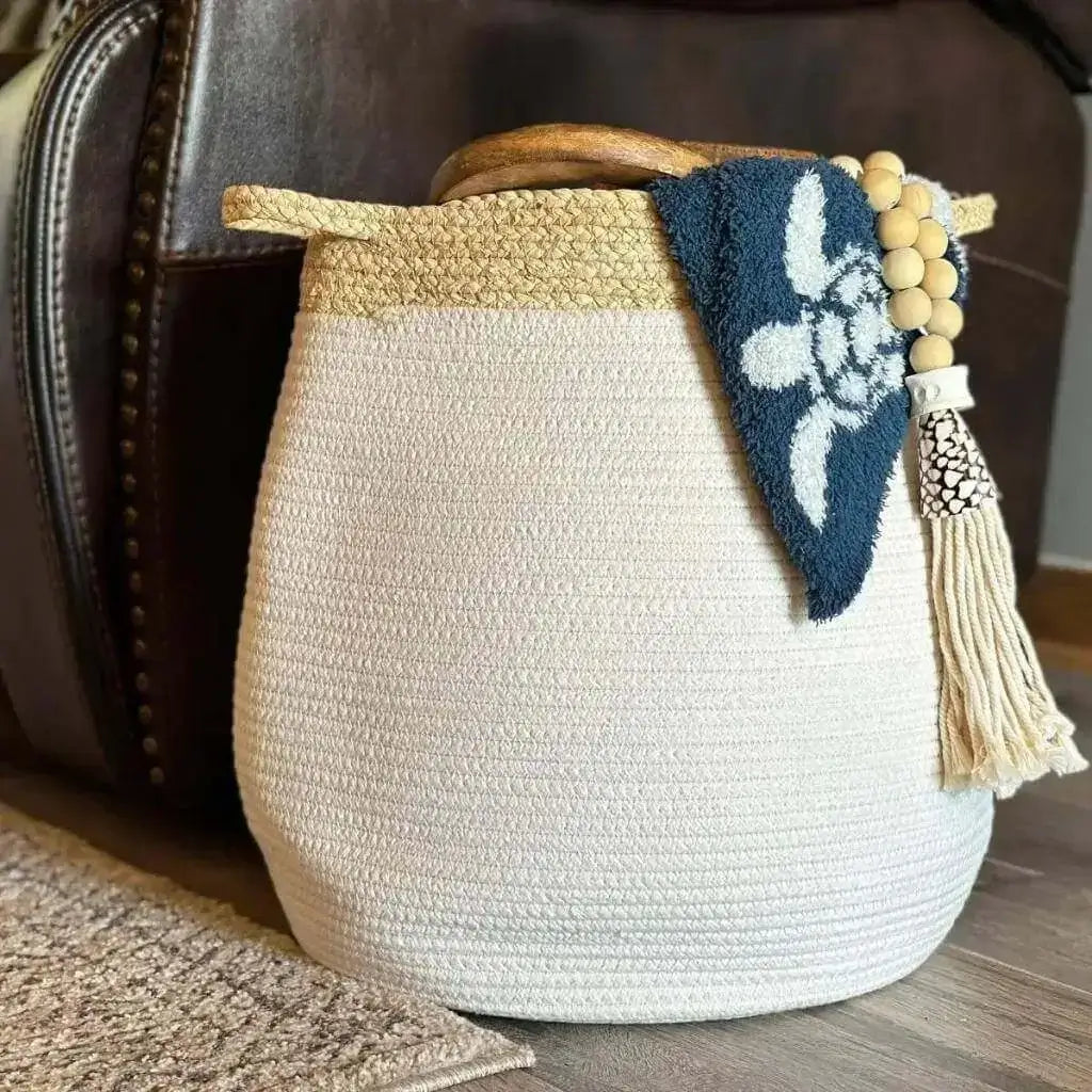 white bell shaped rope basket with corn husk details and handles styled with a blanket by a couch