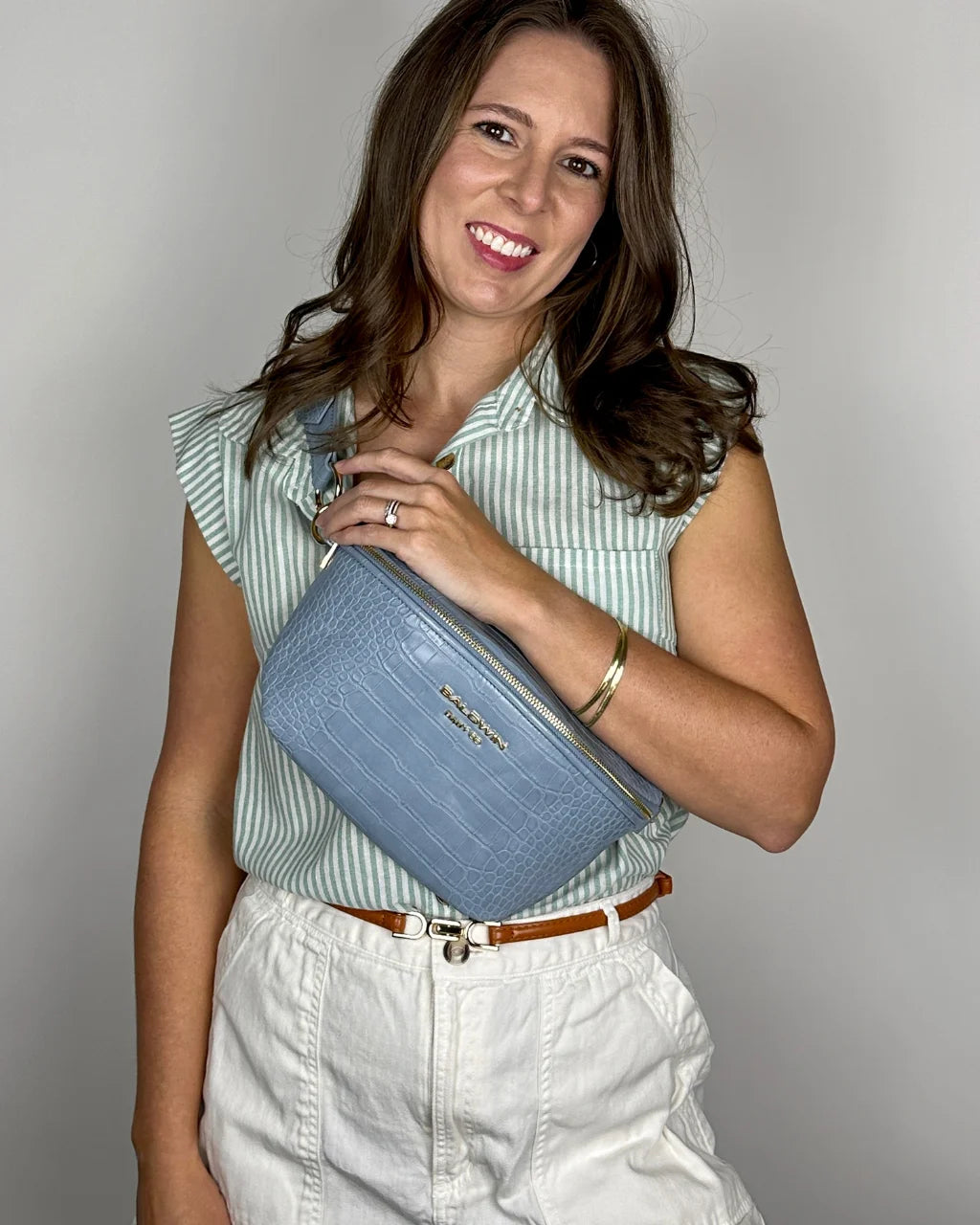 Woman in green and white shirt wearing blue faux croc belt bag crossbody on chest