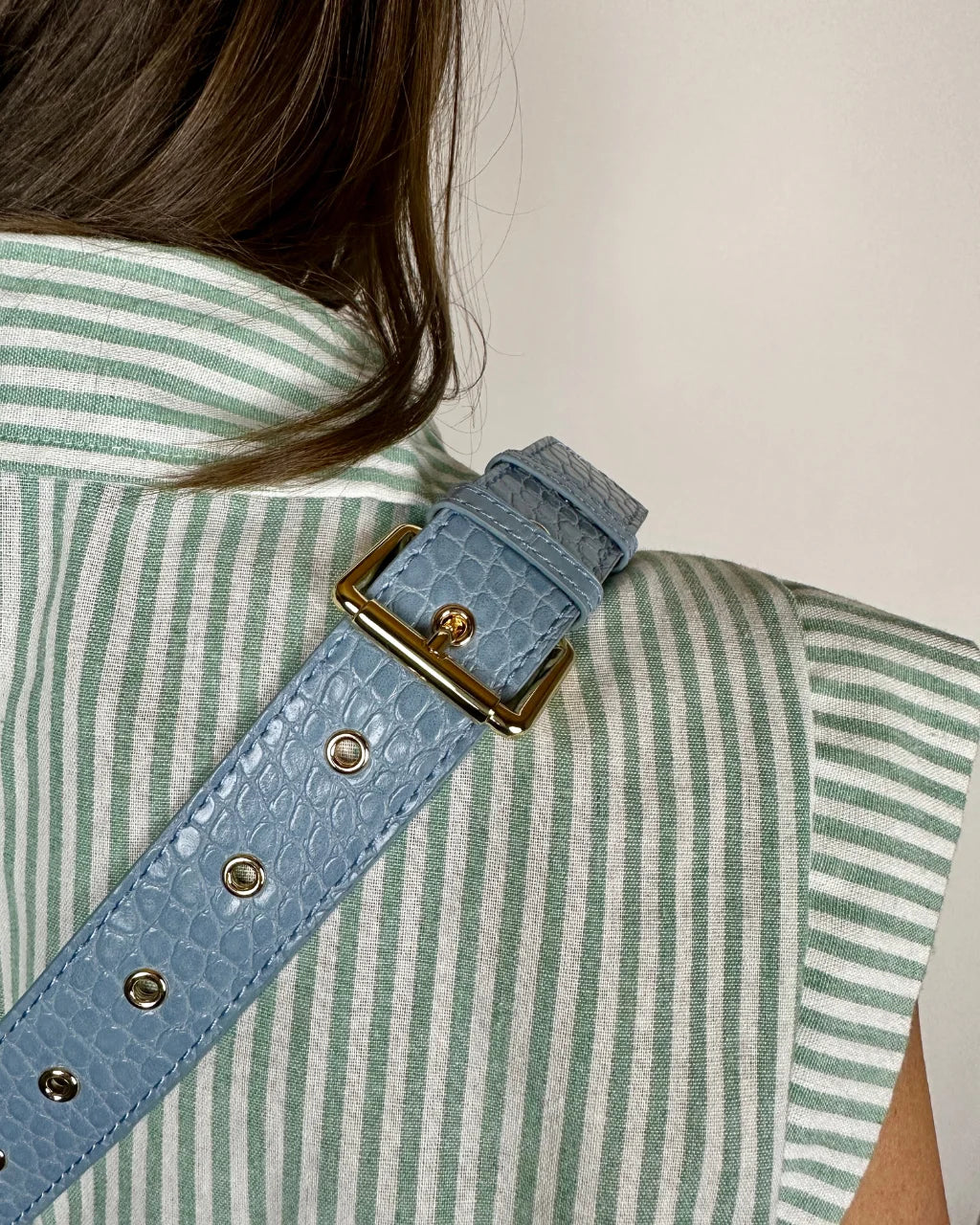 Close-up of blue faux croc belt bag strap with gold eyelets and buckle