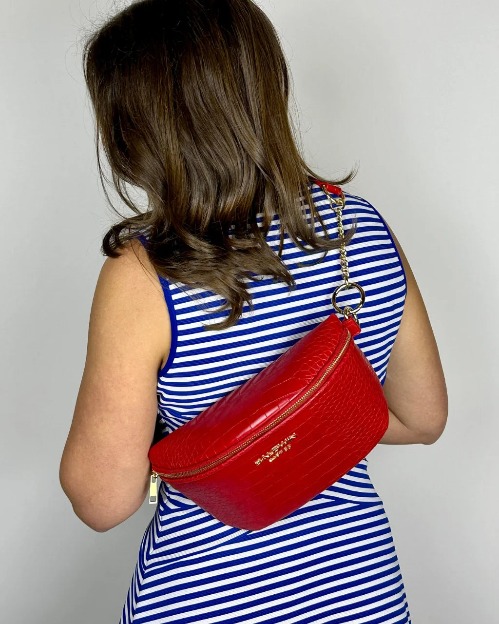 Woman in blue and white dress wearing red faux croc belt bag with gold hardware on back