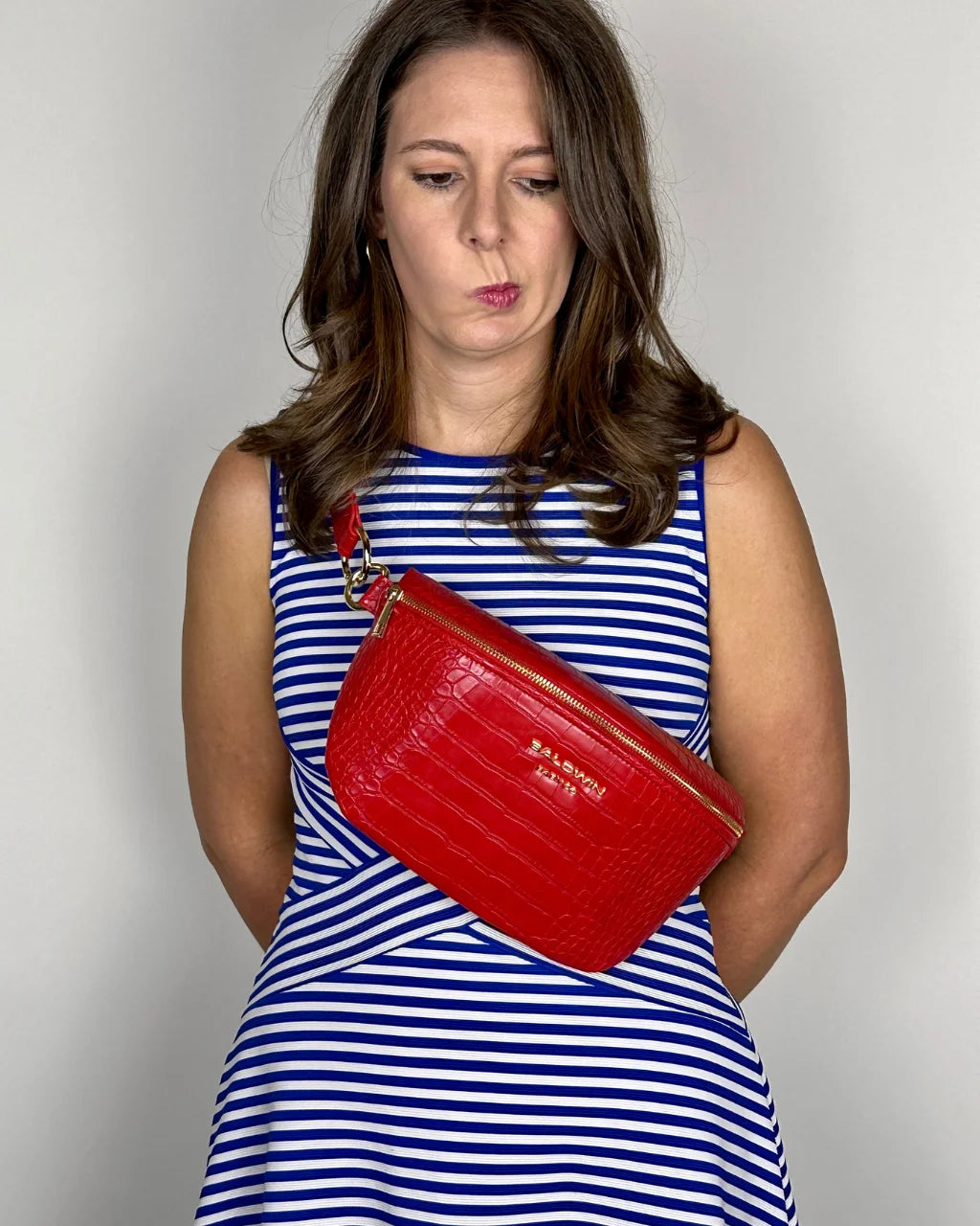 Woman in blue and white dress wearing red faux croc belt bag on chest, showing compact design