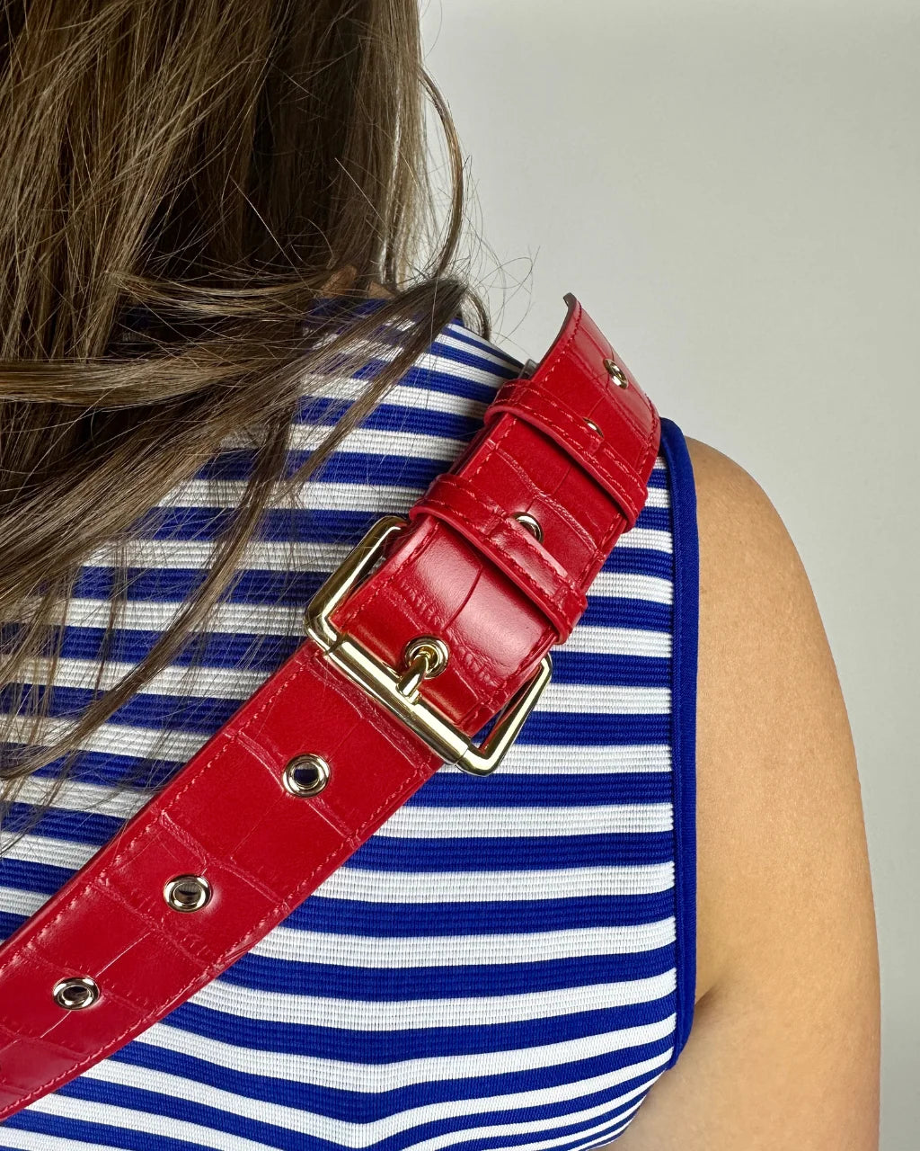 Close-up of red faux croc belt bag strap with gold eyelets and buckle for secure fit