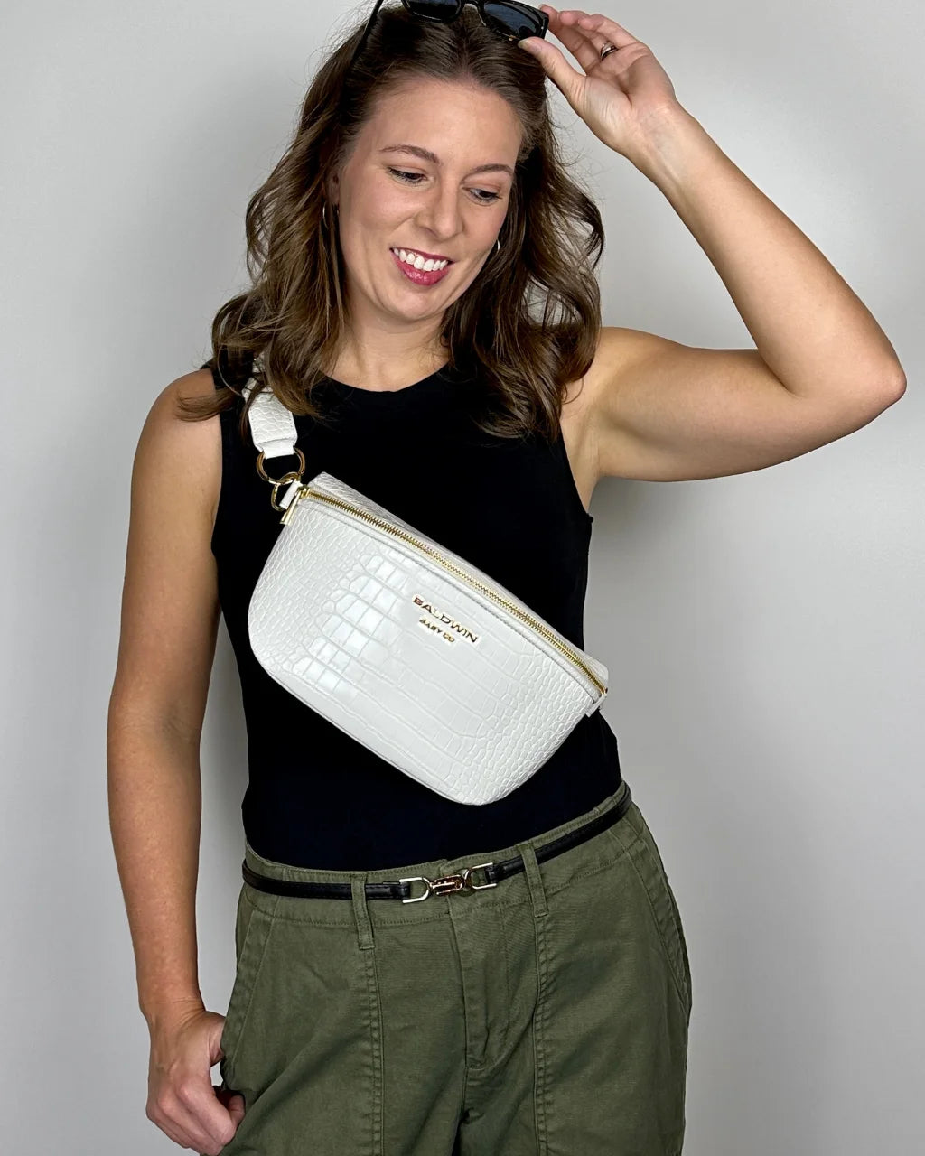 Woman in black shirt and green pants wearing white faux croc belt bag on chest