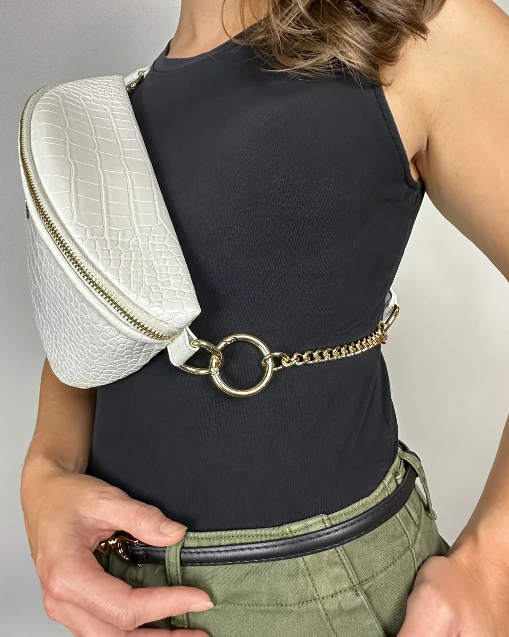 Close-up of gold chain and circular hardware on white faux croc belt bag strap