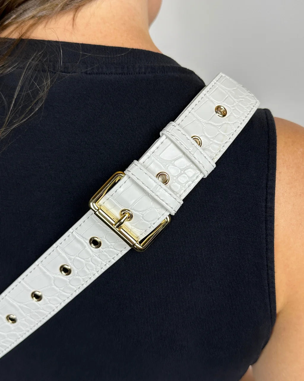 Close-up of white faux croc belt bag strap with gold eyelets and buckle for secure fit