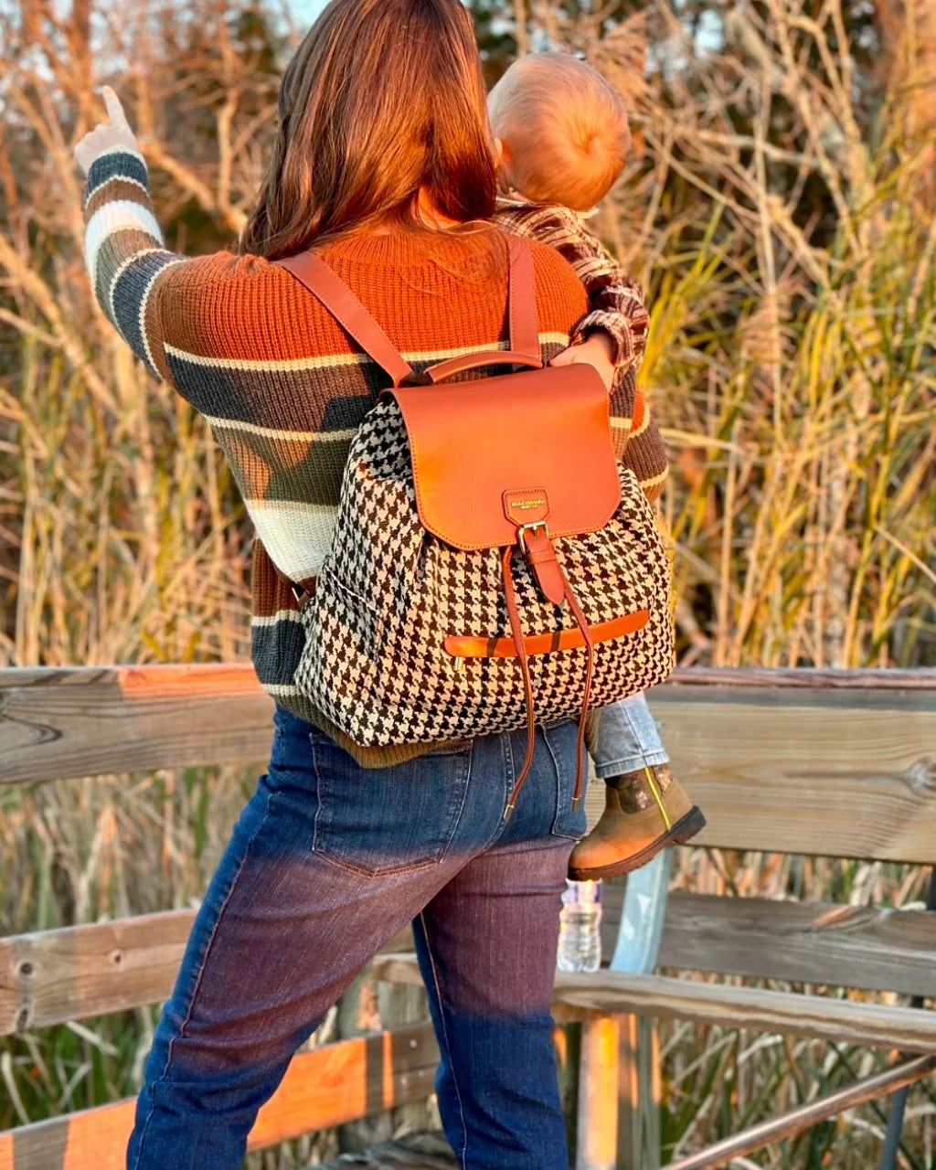 Back view of houndstooth diaper backpack worn by woman holding toddler at sunset
