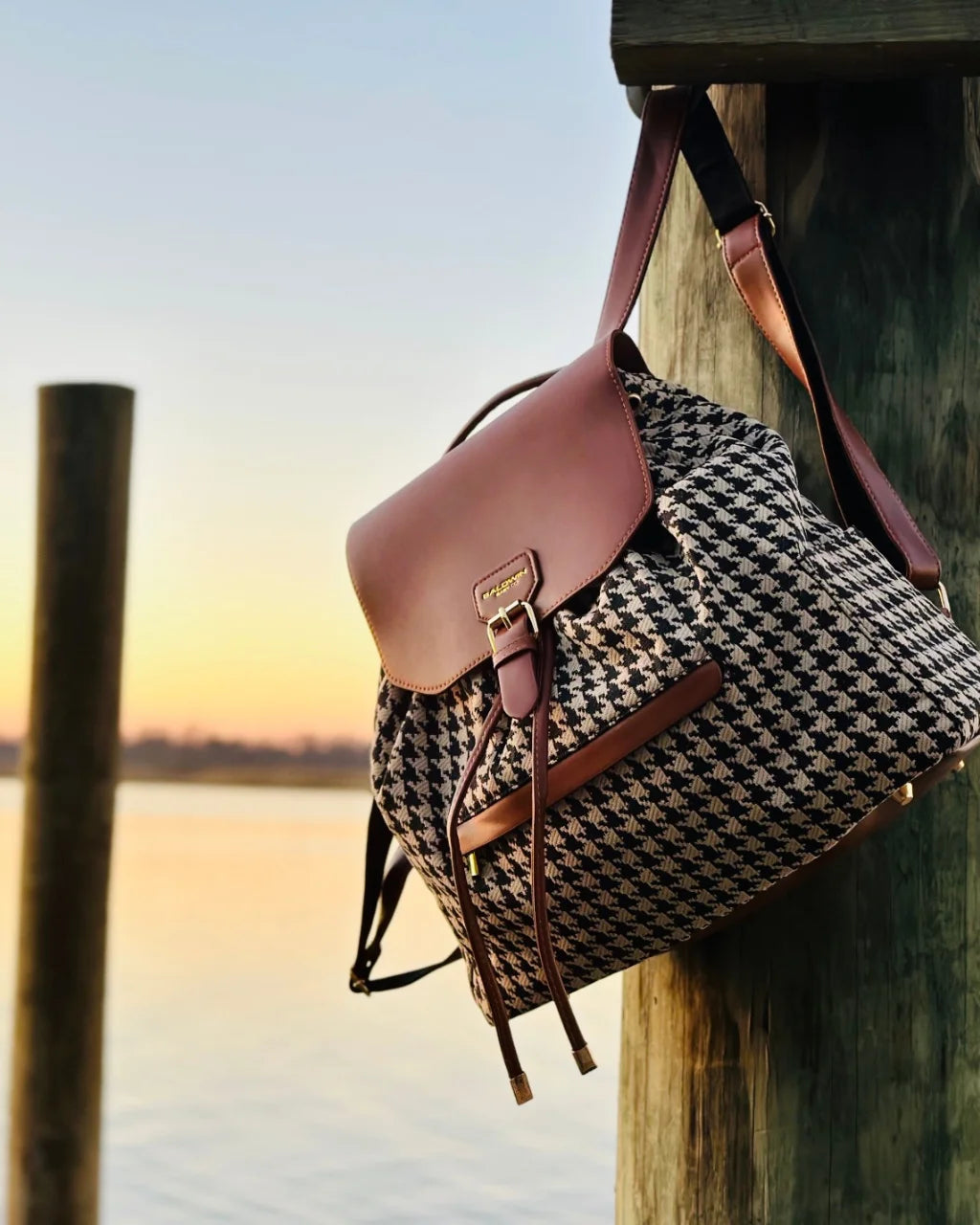 Houndstooth diaper backpack with brown accents hanging on pier post at sunset