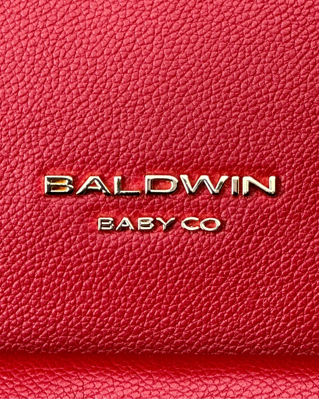 Close-up of gold Baldwin Baby Co logo on textured red vegan leather diaper backpack