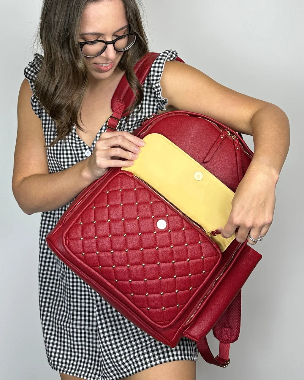 Woman carrying red diaper backpack showing tan lining, spacious design, and style
