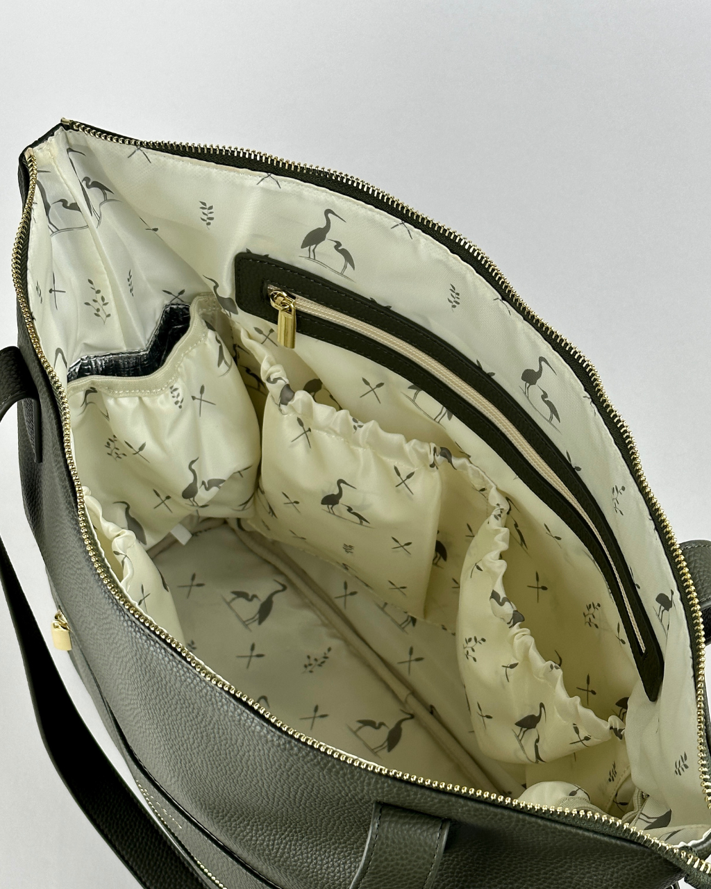 Interior view of the Palmetto Lillian diaper bag, featuring a spacious design with multiple elastic and zippered pockets, lined with elegant heron-themed fabric for stylish organization.
