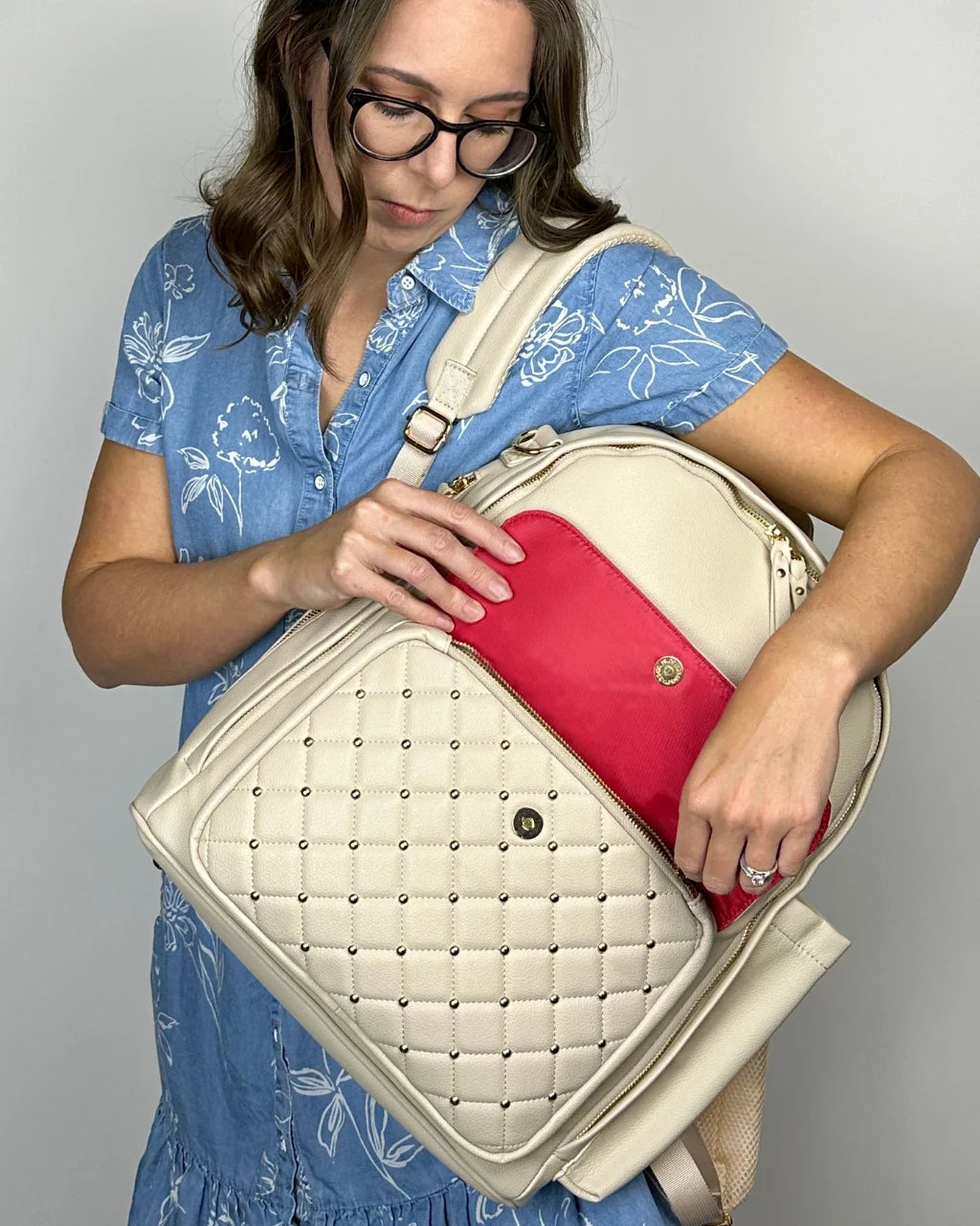 A woman carrying the gray-beige diaper bag backpack in front, emphasizing its red lining, elegant design, and spacious compartments.