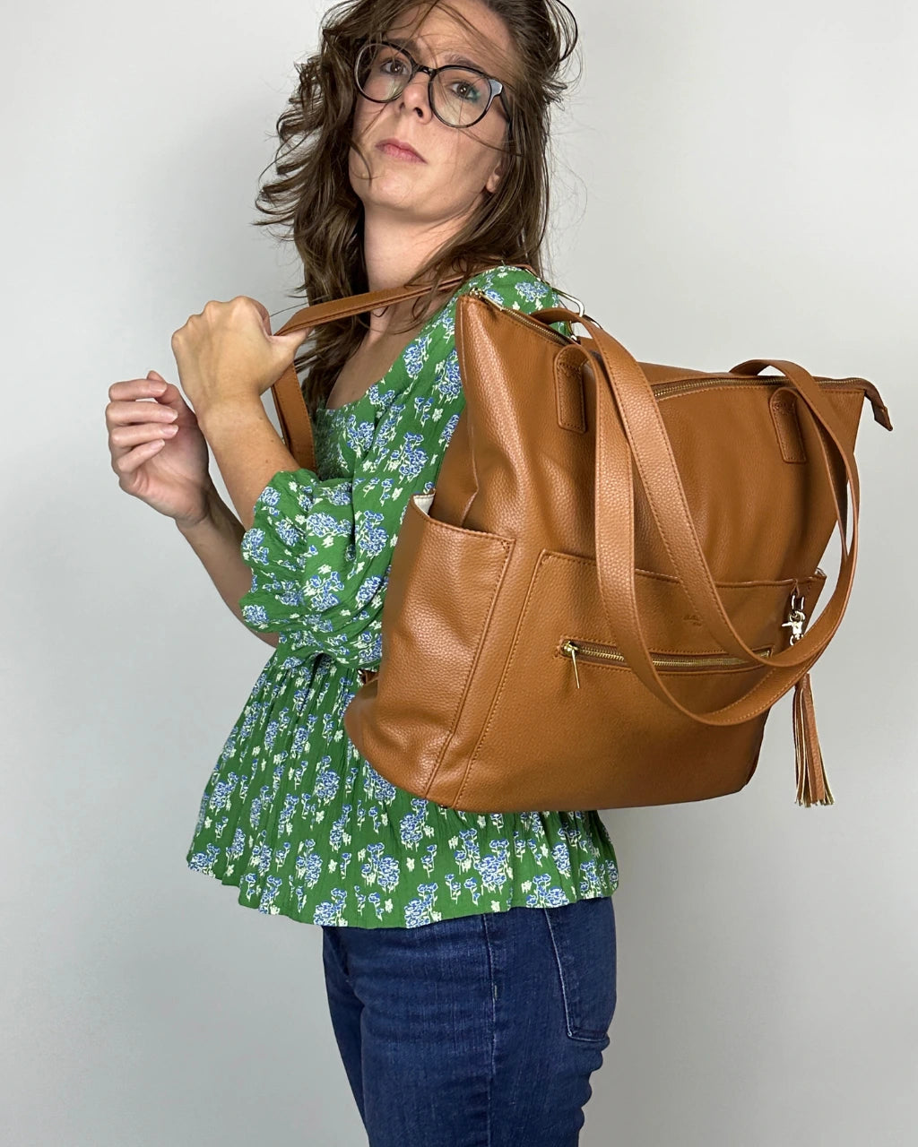 Woman wearing brown leather diaper bag with gold feather and tassel as a backpack