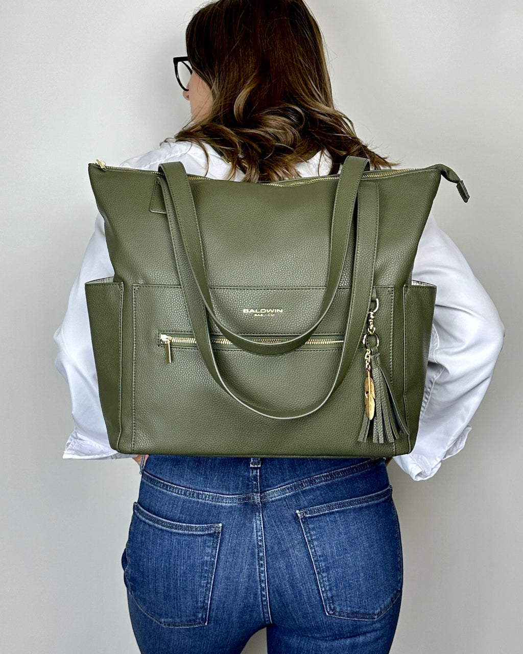 Woman wearing green leather diaper bag with gold feather and tassel as a backpack