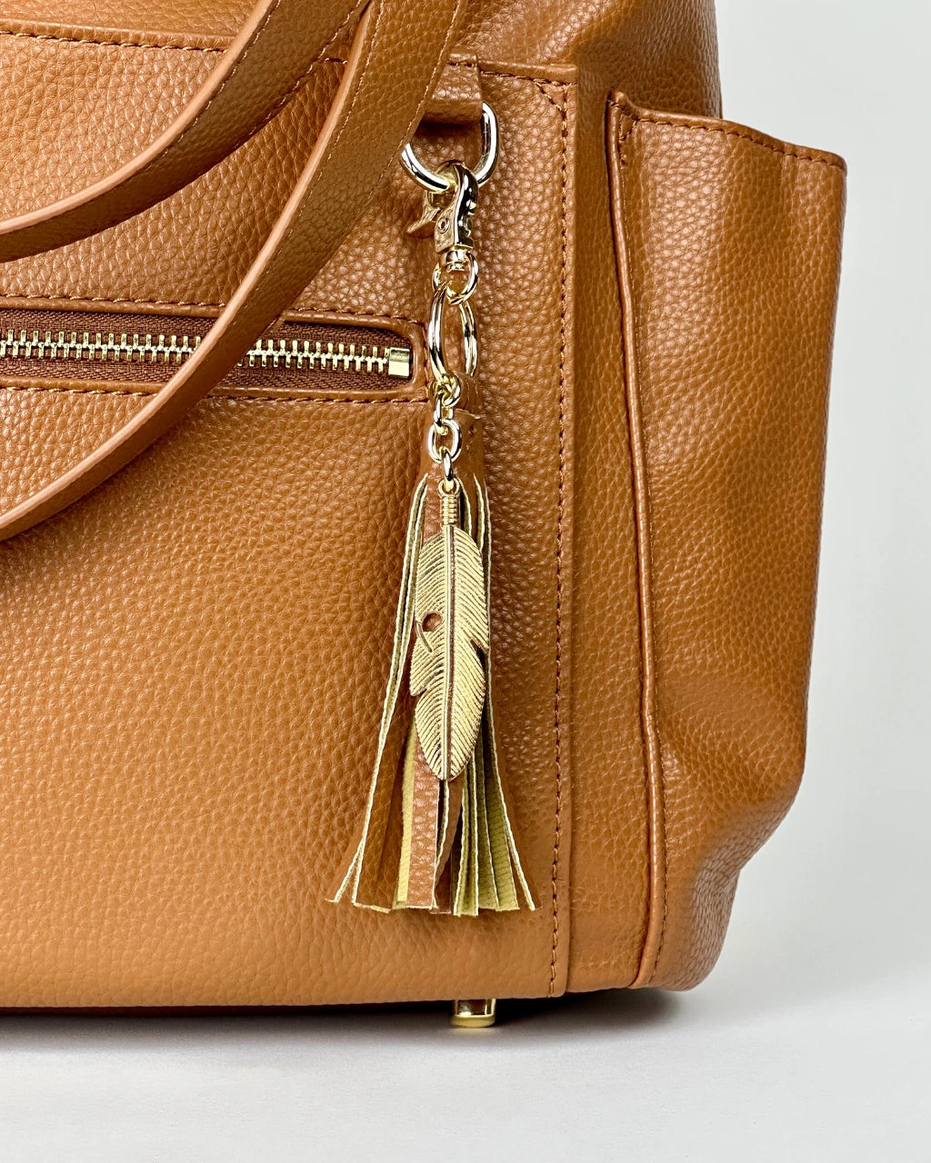 Close up view of vegan brown leather diaper bag with gold feather and tassel