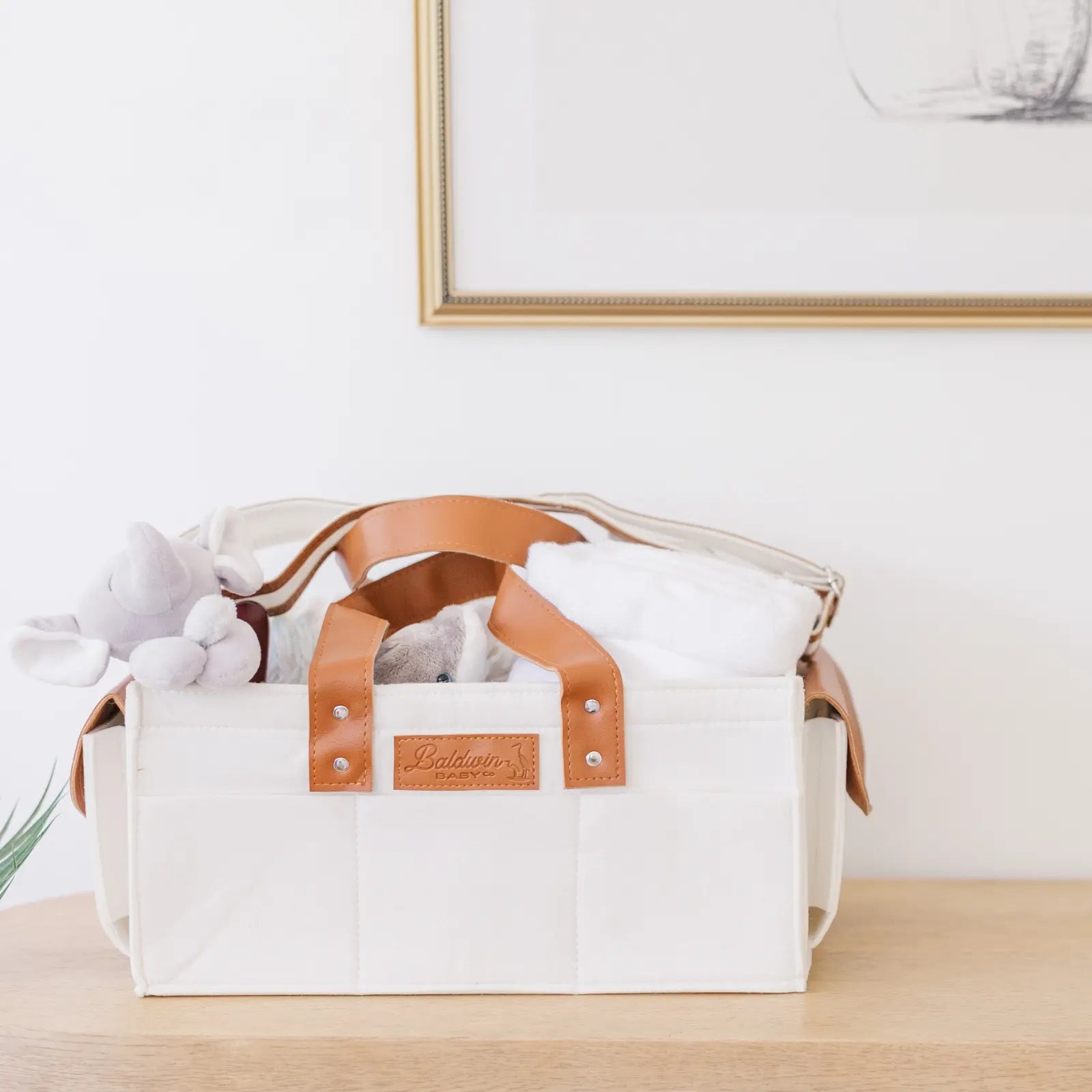 White felt diaper caddy with brown leather handles filled with baby items on wood table