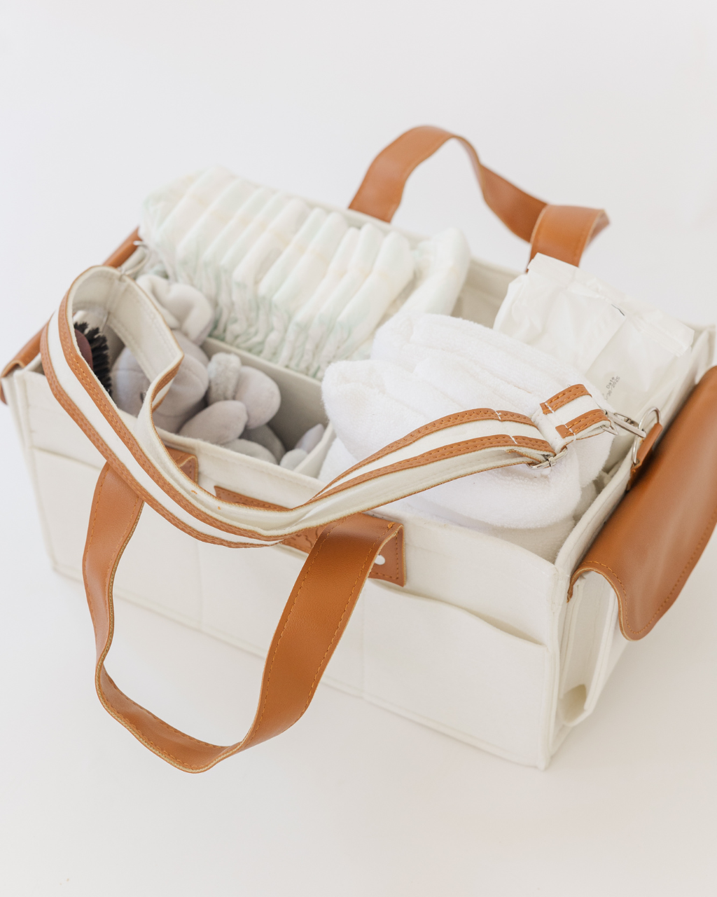 White felt diaper caddy with brown leather handles, filled with baby items