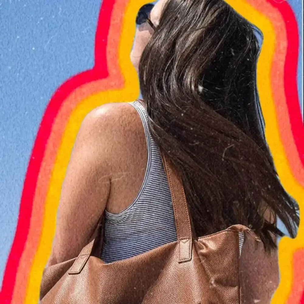 Woman facing away, flipping hair, wearing brown leather bag outlined in yellow, orange, red