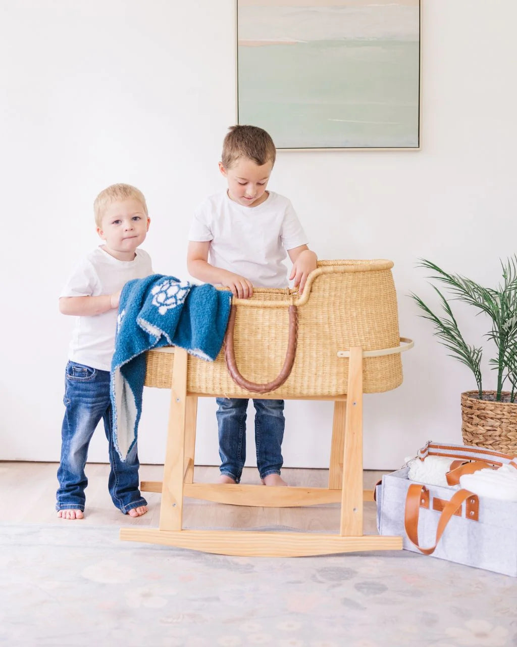 Two boys looking into Moses basket with blue blanket, gray felt diaper caddy nearby