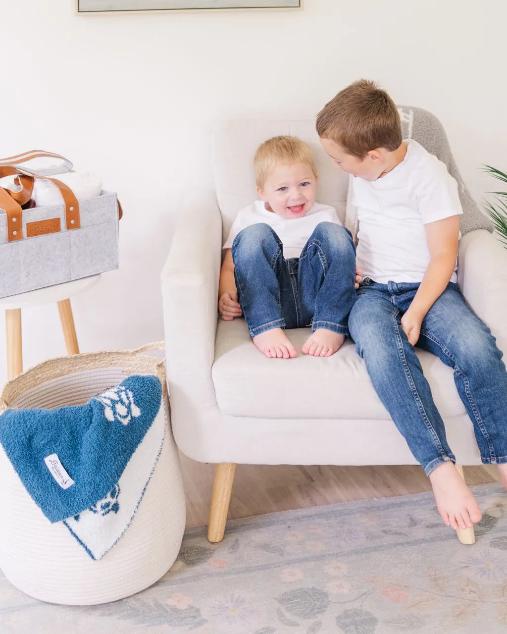 Two boys in chair with white rope basket and blue blanket draped over the side