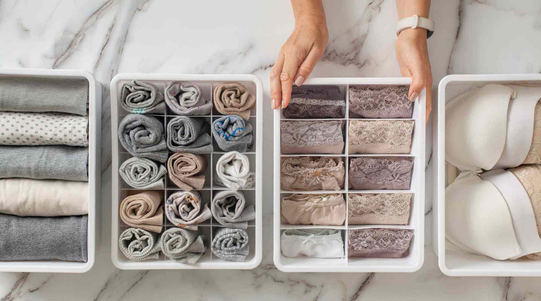 Three storage containers filled with neatly rolled socks, undergarments, and bras. The arrangement is color-coordinated and categorized, showcasing a highly organized system.