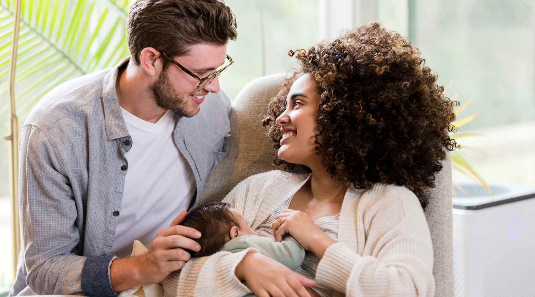 A happy couple sitting together, smiling and gazing at each other while holding their newborn baby, enjoying a peaceful family moment.