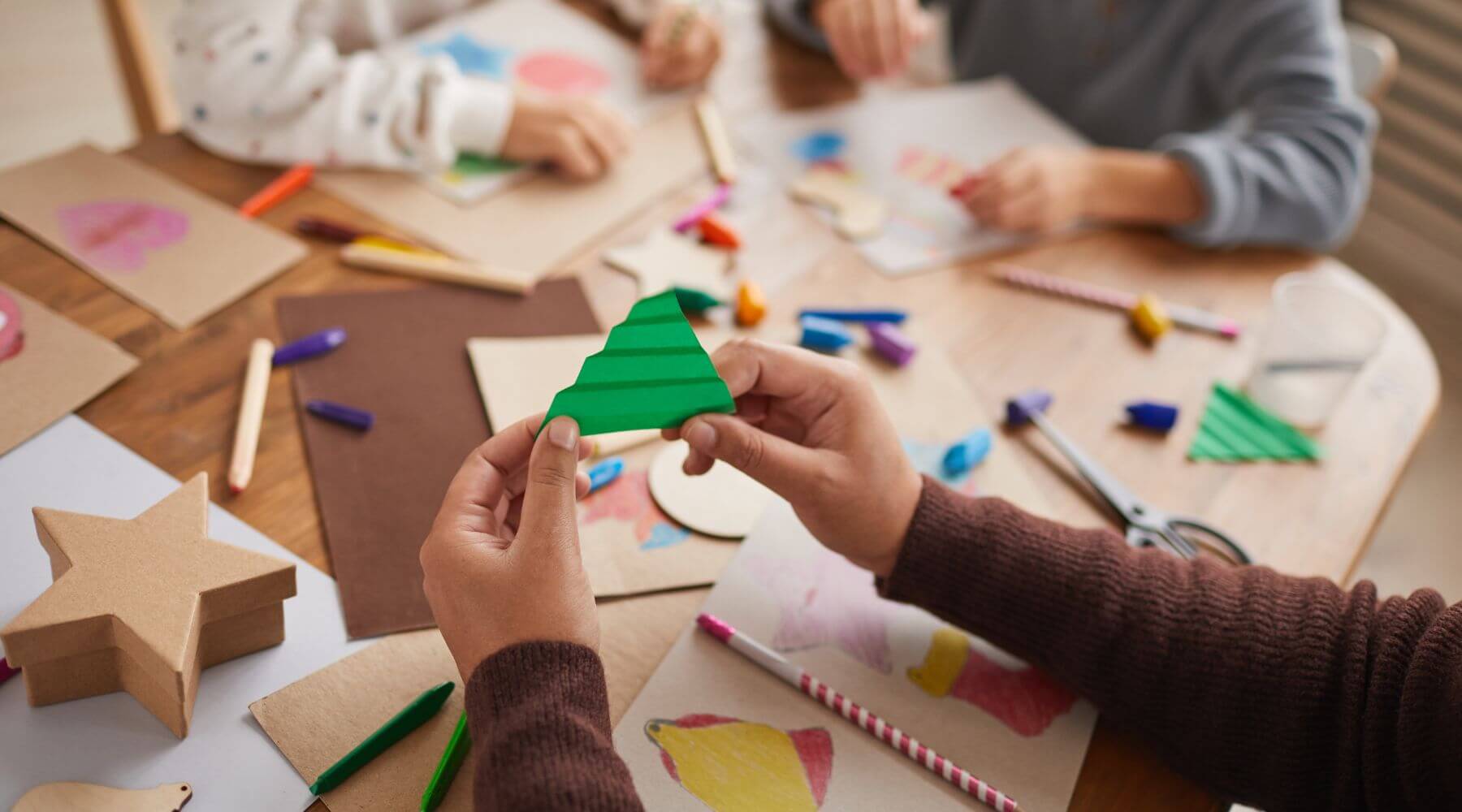 Family Christmas crafting session with paper cutouts, crayons, and handmade tree decorations, ideal for festive family bonding time