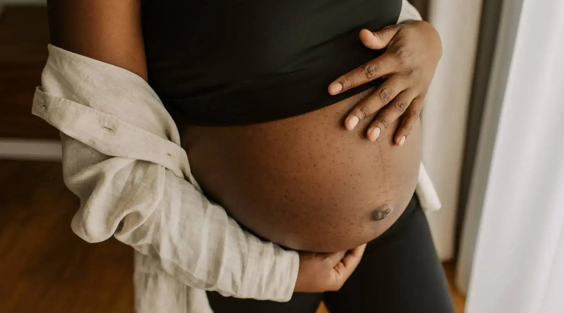 Close-up of pregnant woman’s bare belly with hands resting gently, symbolizing motherhood and pregnancy joy.